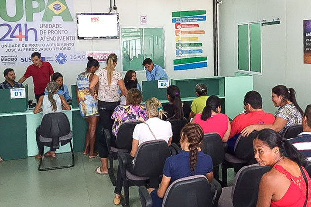 Na foto várias pessoas estão na recepção da UPA Trapiche, todas de costas para a câmera. Algumas sentadas e outras em frente ao guichê de informações.