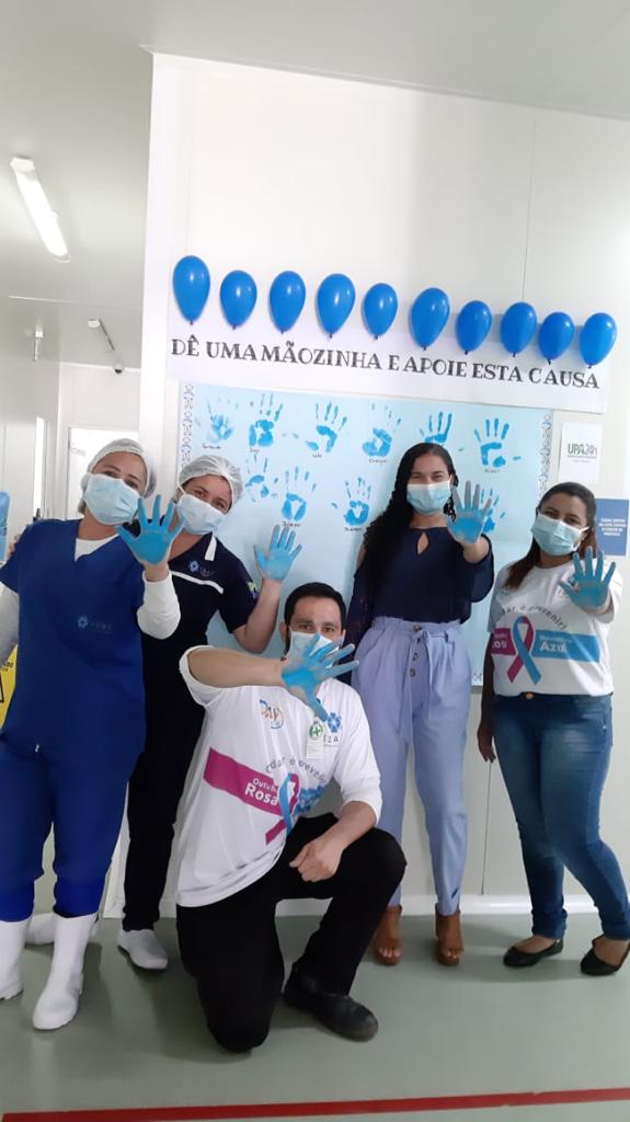 Cinco colaboradores da UPA mostram a mão pintada de azul. Eles estão de frente para a câmera, sendo que um deles está agachado. Atrás, há um painel branco com a marca de várias mãos na cor azul. Em cima do painel há balões azuis e a frase "dê uma mãozinha e apoie essa causa".